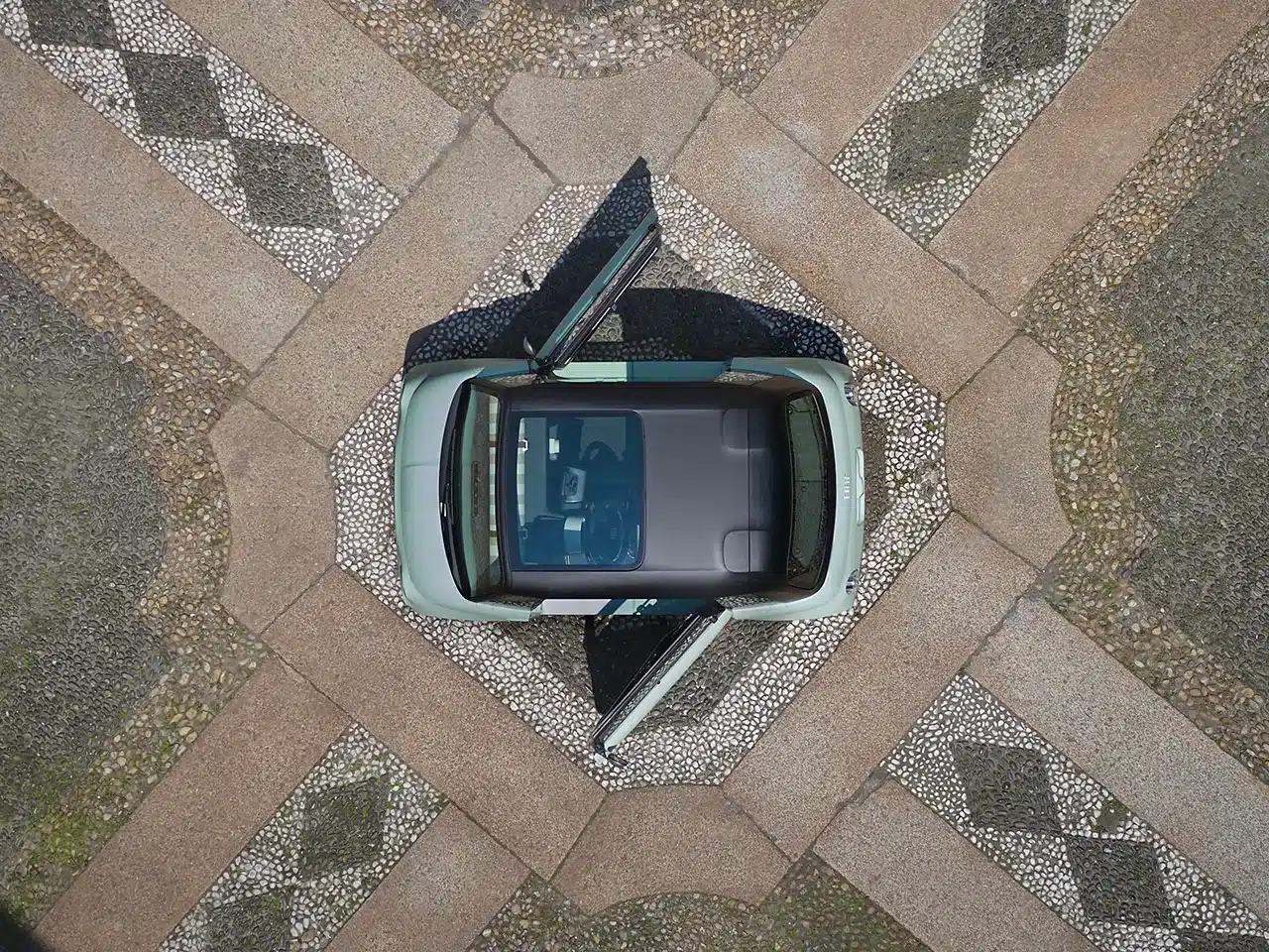 Fiat Topolino in Grün aus der Vogelperspektive mit geöffneten Türen auf gepflastertem Platz.