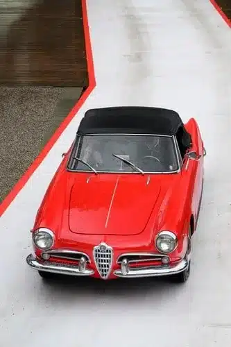 Roter Alfa Romeo Spider Cabrio von oben auf einer Straße, klassisches Liebhaberfahrzeug mit schwarzem Verdeck.