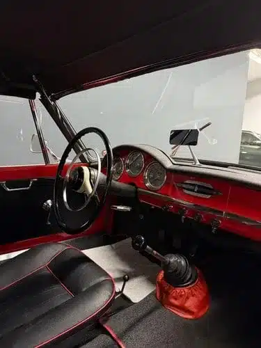 Blick in den Fahrzeuginnenraum eines Oldtimers, rote Armaturen, klassische Instrumente und Schaltknauf sichtbar