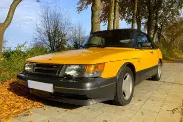 Gelber Youngtimer-Cabrio-Oldtimer steht auf herbstlicher Allee, gepflegter Zustand, klassische Linienführung.