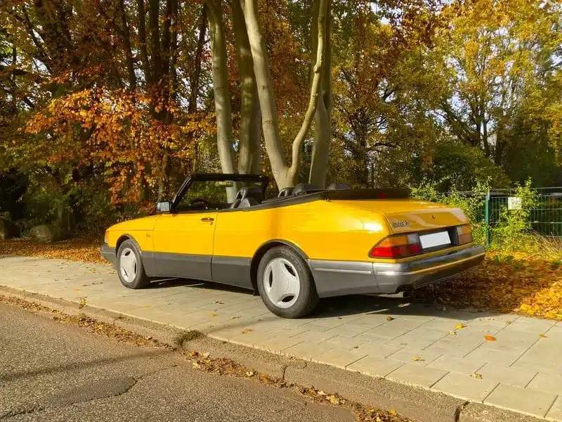 Gelber Saab 900 Cabrio geparkt im Herbstlaub, Ansicht von hinten seitlich