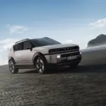 SUV fährt auf einem weiten Sandstrand mit blauem Himmel und Küste im Hintergrund