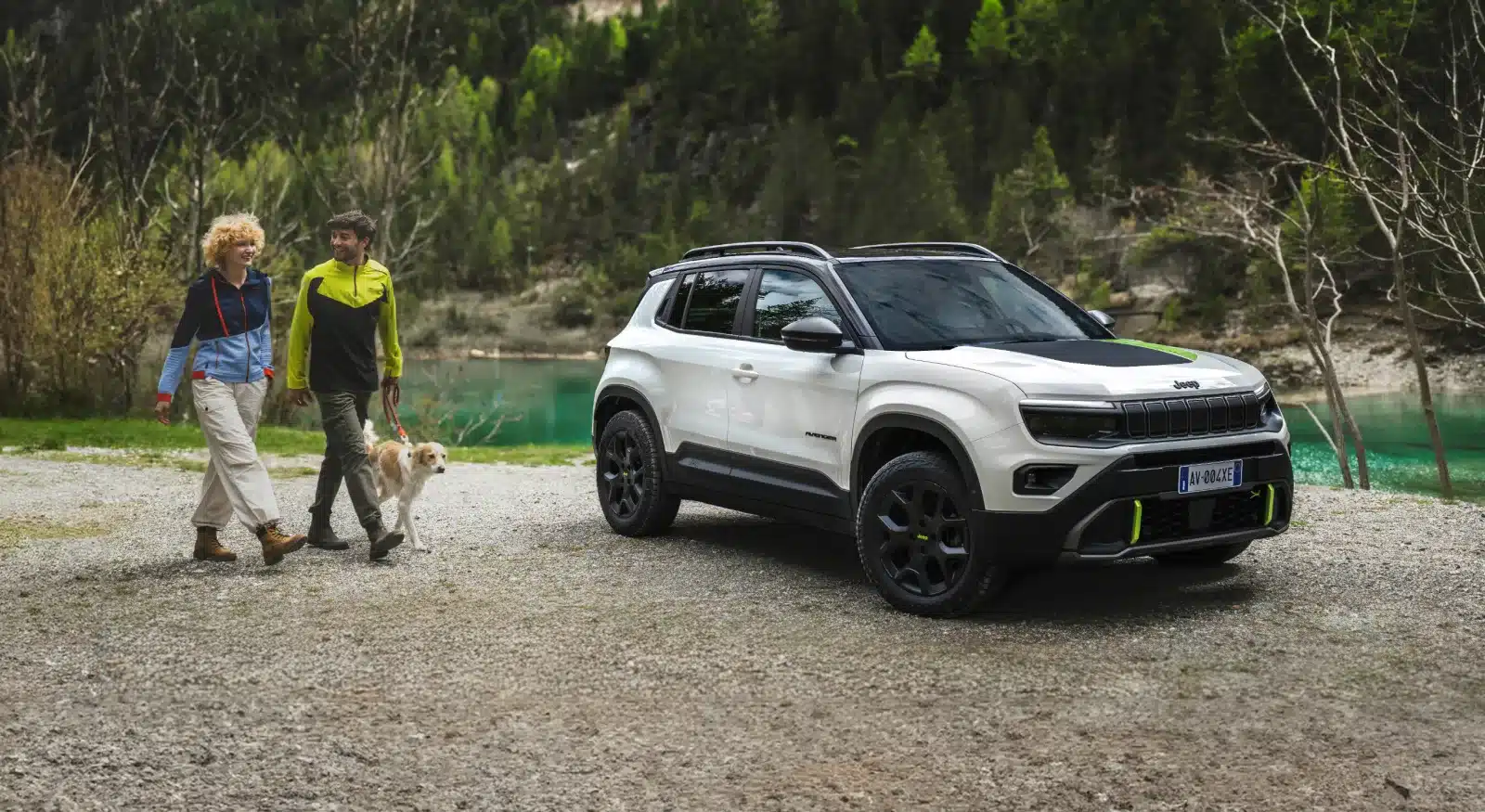 Jeep Avenger 4xe Hybrid in weiß-schwarzer Lackierung nahe eines Sees, mit Spaziergängern und Hund im Vordergrund.