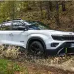 Weißer Jeep Avenger 4xe Hybrid fährt durch eine matschige Pfütze im Wald