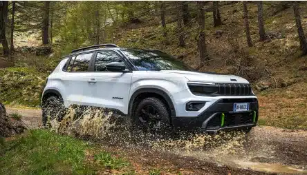 Weißer Jeep Avenger 4xe Hybrid fährt durch eine matschige Pfütze im Wald