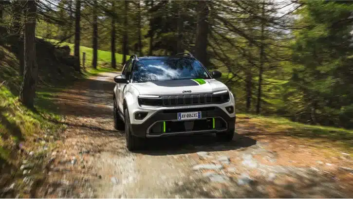 Jeep Avenger 4xe Hybrid fährt auf einem Waldweg, umgeben von Bäumen.