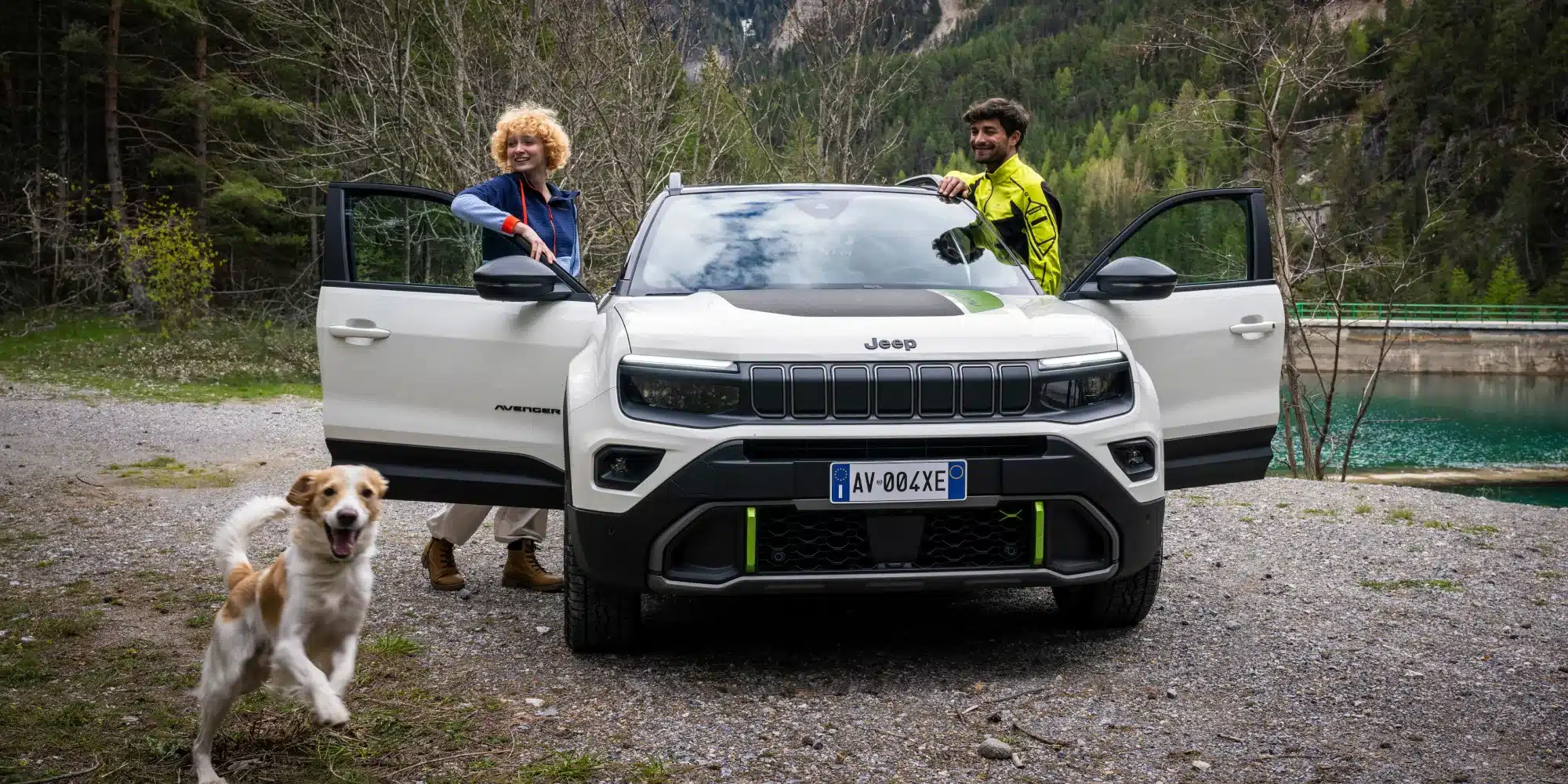 Jeep Avenger 4xe Hybrid mit zwei Personen und Hund vor Fluss und Wald