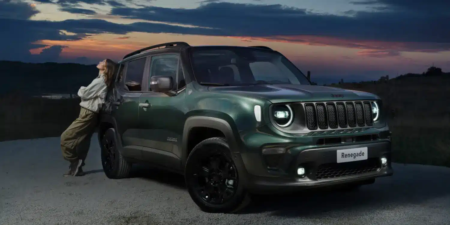 Grüner Jeep Renegade e-Hybrid mit einer Person am Fahrzeug vor abendlicher Landschaft.