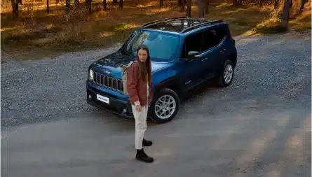Jeep Renegade e-Hybrid in dunkelblau, geparkt auf einem Waldweg, daneben steht eine Person.