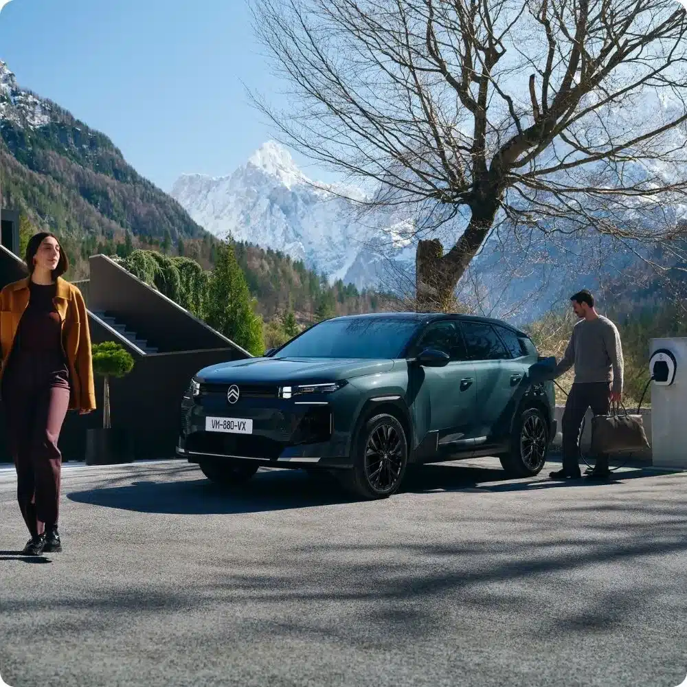 Citroën C5 Aircross wird an einer Ladesäule geladen, im Hintergrund verschneite Berge und zwei Personen.
