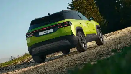 Grüner Jeep Compass e-Hybrid von hinten auf unbefestigtem Weg, demonstriert Offroad-Fähigkeiten im Gelände.