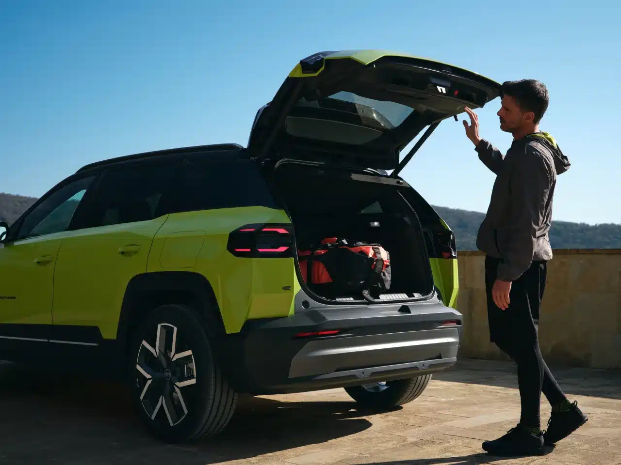 Mann öffnet den Kofferraum eines Jeep Compass e-Hybrid, beladen mit Taschen.