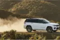 Weißer Jeep Grand Cherokee 4xe fährt auf einer staubigen Piste durch hügelige Landschaft.
