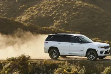 Weißer Jeep Grand Cherokee 4xe fährt auf einer staubigen Piste durch hügelige Landschaft.