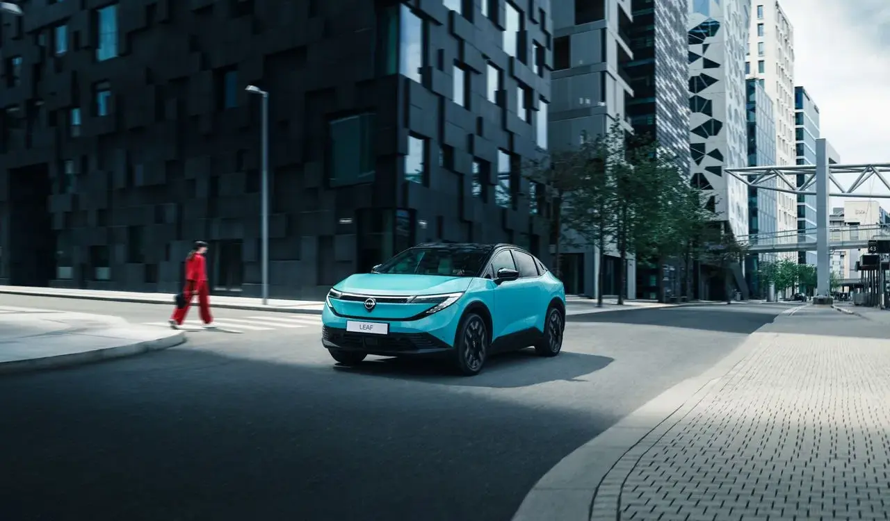 Nissan LEAF 2024 in türkis auf einer Straße vor modernen Hochhäusern.