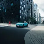 Nissan LEAF 2024 in türkis auf einer Straße vor modernen Hochhäusern.