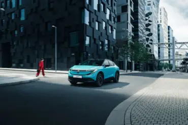 Nissan LEAF 2024 in türkis auf einer Straße vor modernen Hochhäusern.