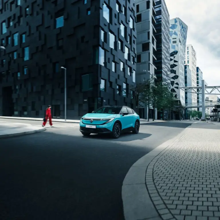 Nissan LEAF 2024 in türkis auf einer Straße vor modernen Hochhäusern.