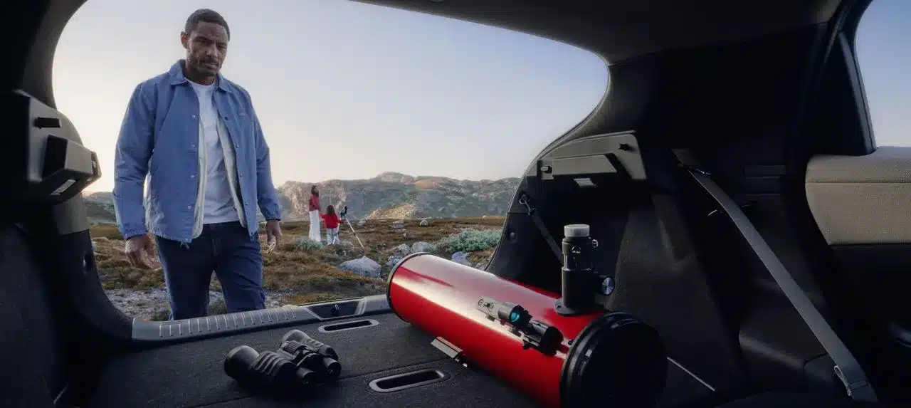 Blick in den großzügigen Kofferraum eines Nissan LEAF, darin ein Fernglas und ein Teleskop, im Hintergrund Personen in der Natur