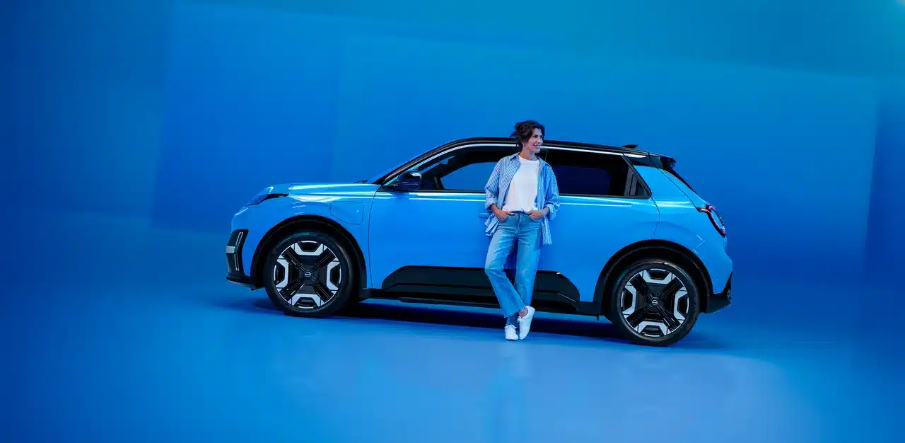 Frau steht an einem leuchtend blauen Elektroauto in einer minimalistischen Studioumgebung