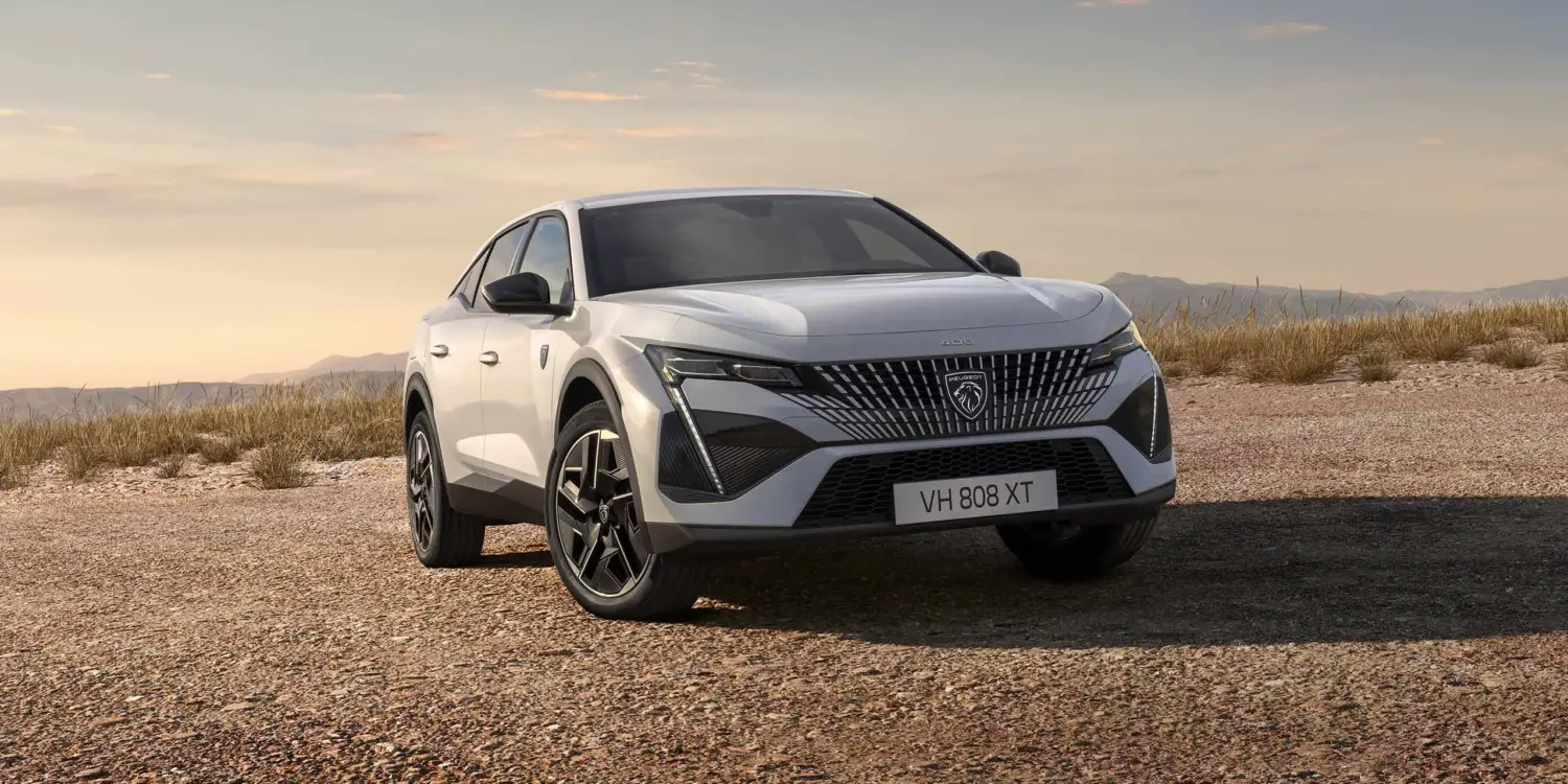 Der neue Peugeot E-408 als vollelektrisches Fastback-Modell in weißer Lackierung auf offenem Gelände vor bergiger Kulisse.