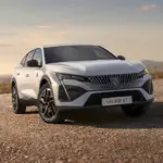 Der neue Peugeot E-408 als vollelektrisches Fastback-Modell in weißer Lackierung auf offenem Gelände vor bergiger Kulisse.