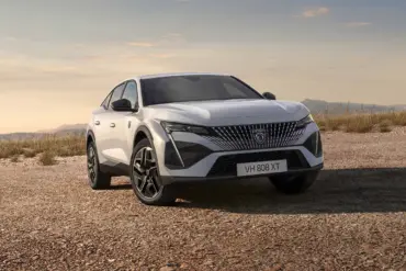 Der neue Peugeot E-408 als vollelektrisches Fastback-Modell in weißer Lackierung auf offenem Gelände vor bergiger Kulisse.