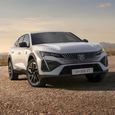 Der neue Peugeot E-408 als vollelektrisches Fastback-Modell in weißer Lackierung auf offenem Gelände vor bergiger Kulisse.