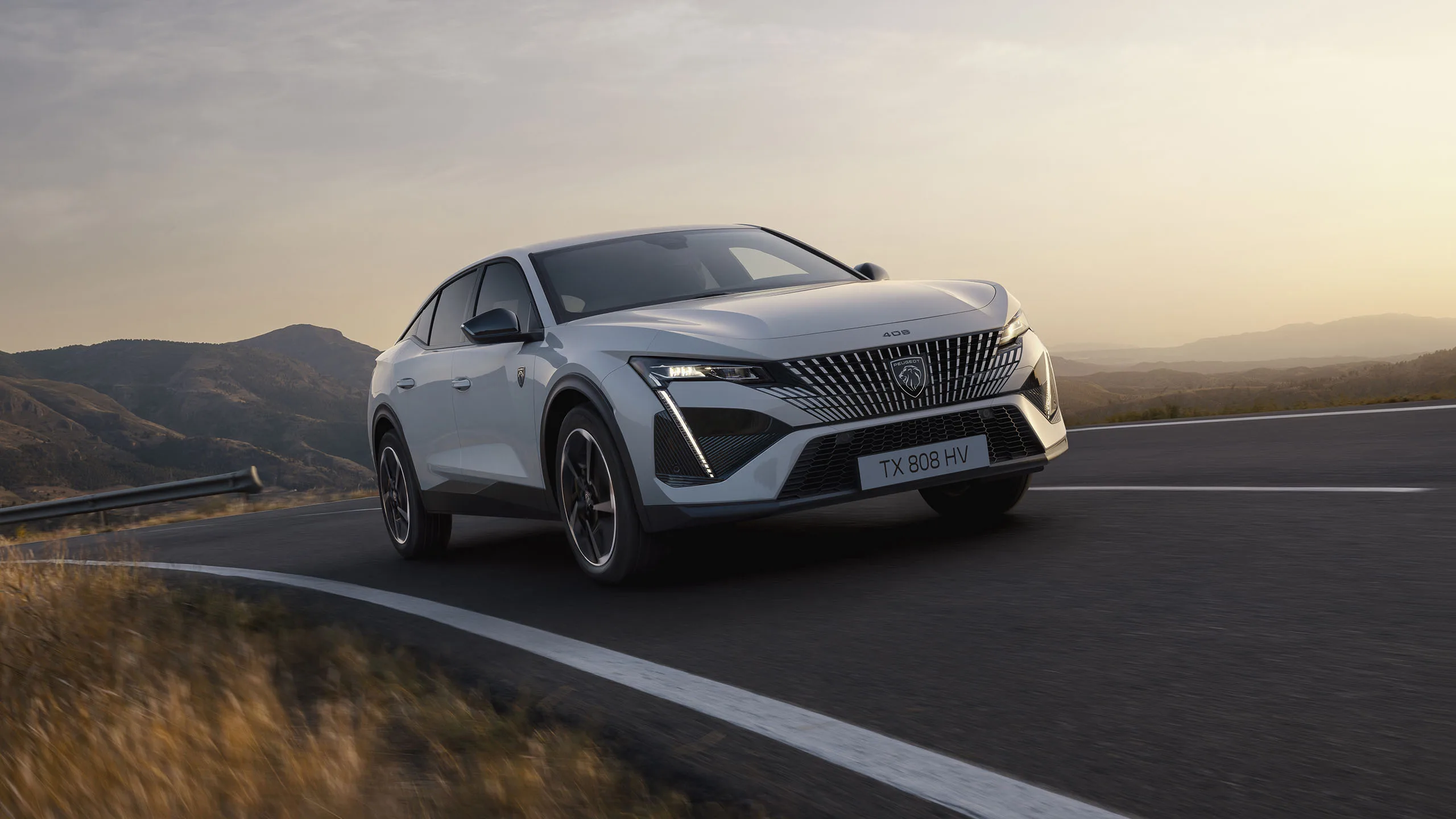 Peugeot E-408 vollelektrisch auf kurviger Landstraße bei Sonnenuntergang