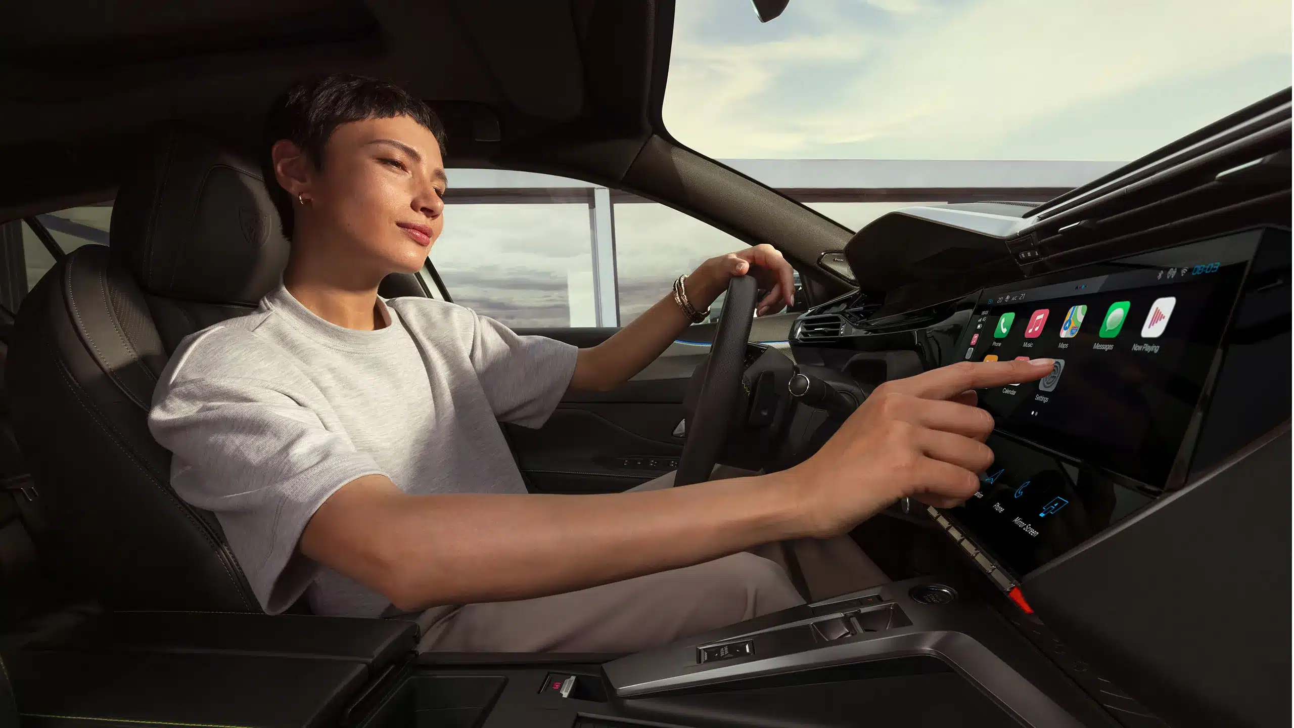 Innenansicht des Peugeot E-408 mit Fahrerin am Touchscreen des digitalen i-Cockpits