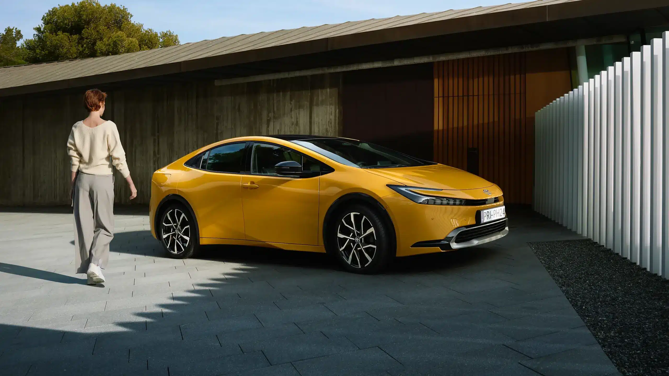 Neuer Toyota Prius Plug-in Hybrid in Gelb, geparkt vor einem modernen Gebäude, seitliche Ansicht.