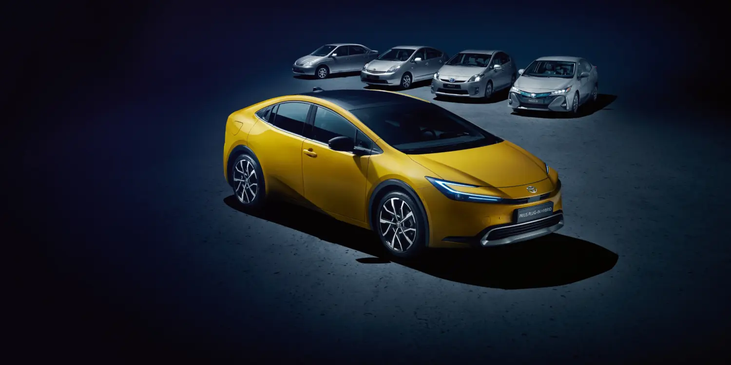 Toyota Prius Plug-in Hybrid in Gelb, umgeben von älteren Prius-Generationen, auf dunklem Untergrund.