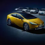 Toyota Prius Plug-in Hybrid in Gelb, umgeben von älteren Prius-Generationen, auf dunklem Untergrund.