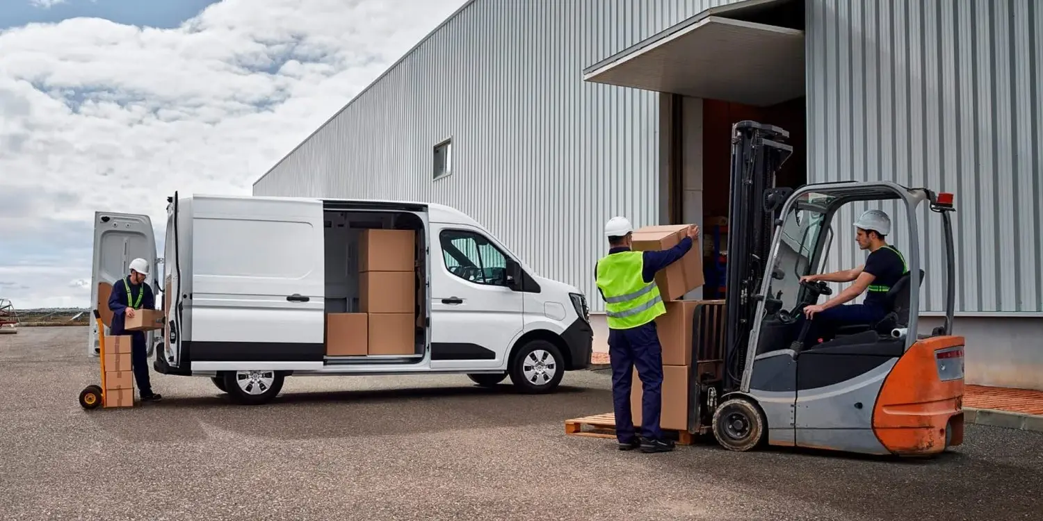 Nissan Interstar Transporter wird vor einer Lagerhalle von mehreren Personen mit Kartons beladen, ein Gabelstapler unterstützt den Vorgang.