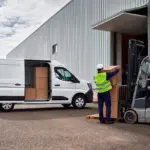 Nissan Interstar Transporter wird vor einer Lagerhalle von mehreren Personen mit Kartons beladen, ein Gabelstapler unterstützt den Vorgang.