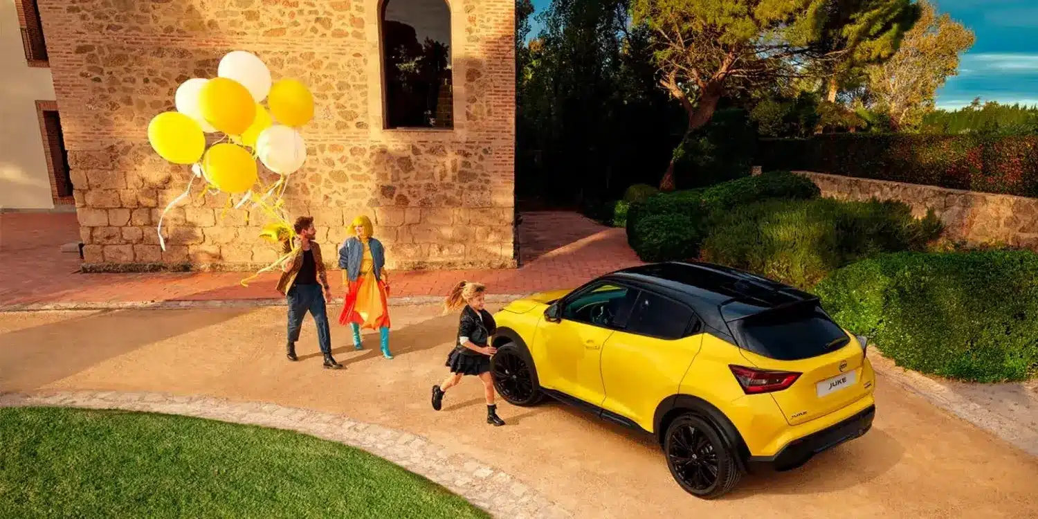 Gelber Nissan Juke mit schwarzem Dach vor Steinmauer und Personen mit gelben und weißen Ballons.