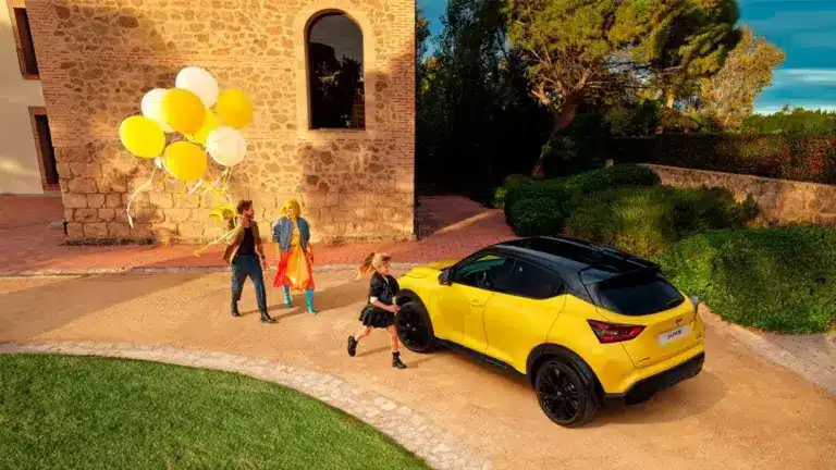 Gelber Nissan Juke mit schwarzem Dach vor Steinmauer und Personen mit gelben und weißen Ballons.