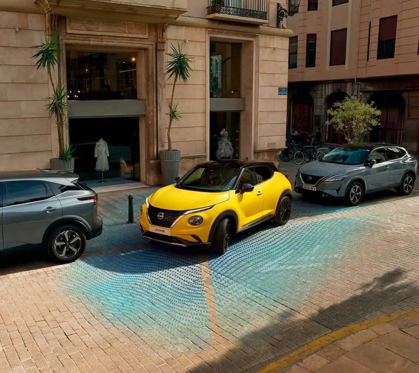 Gelber Nissan Juke, der mit Einparkhilfe zwischen zwei Autos in einer Stadt parkt.