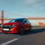 Nissan Qashqai e-POWER in Rot fährt auf einer Straße mit Brücke im Hintergrund.