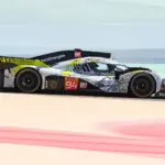 Peugeot 9X8 Hypercar auf der Rennstrecke mit auffälliger Art-Car-Lackierung in Grau, Gelbgrün und Schwarz, seitlich aufgenommen.