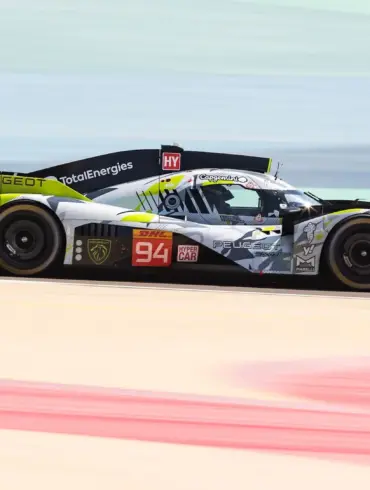 Peugeot 9X8 Hypercar auf der Rennstrecke mit auffälliger Art-Car-Lackierung in Grau, Gelbgrün und Schwarz, seitlich aufgenommen.