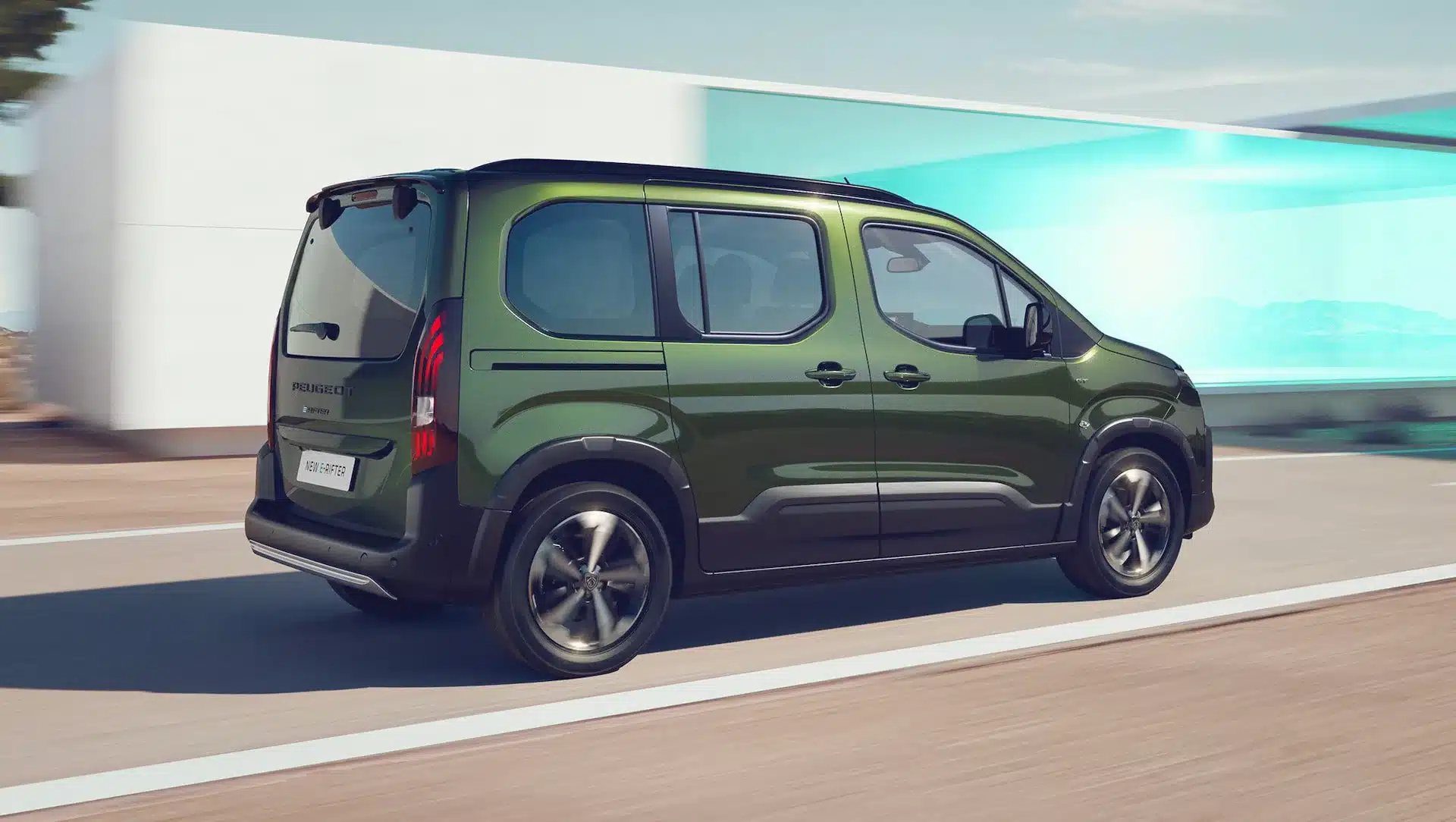 Grüner Peugeot E-Rifter fährt auf einer modernen Straße, sichtbare Rückansicht des Elektro-Vans.