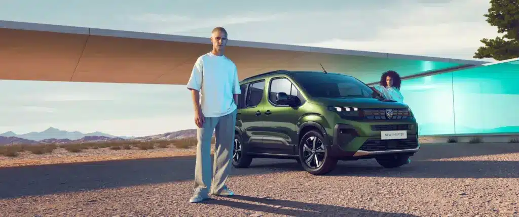 Grüner Peugeot E-Rifter Elektro-Van vor moderner Architektur und Berglandschaft, mit zwei Personen im Bild.