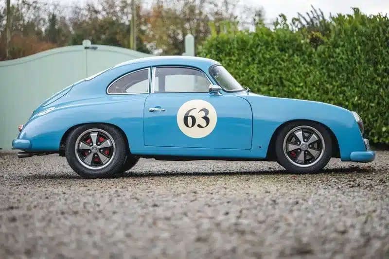 Blauer Porsche 356 Outlaw Tribute mit Startnummer 63 von der Seite auf Schotter stehend.