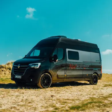 Renault Master VANtastic Campervan steht auf sandigem Gelände unter blauem Himmel.