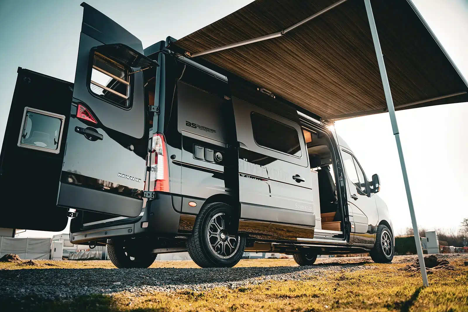 Der Renault Master VANtastic als Campervan mit offener Seitentür und geöffneter Hecktür unter einer aufgebauten Markise.