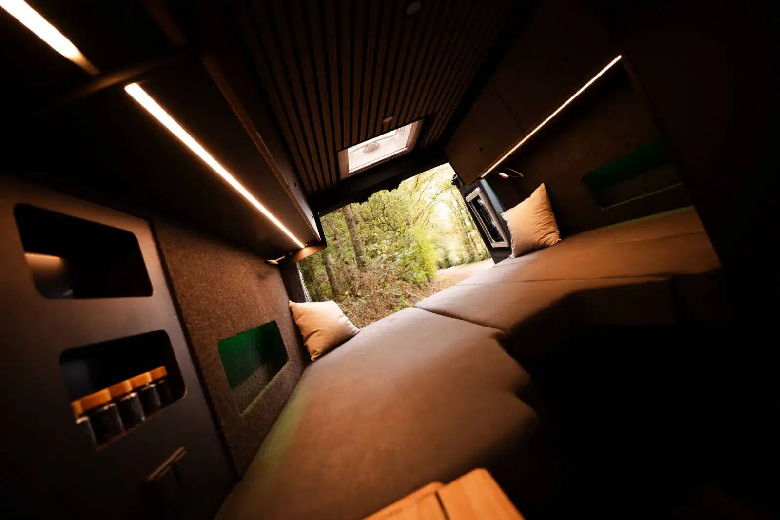 Längsbett im Renault Master VANtastic Camper, gemütlich beleuchtet mit Blick nach draußen.