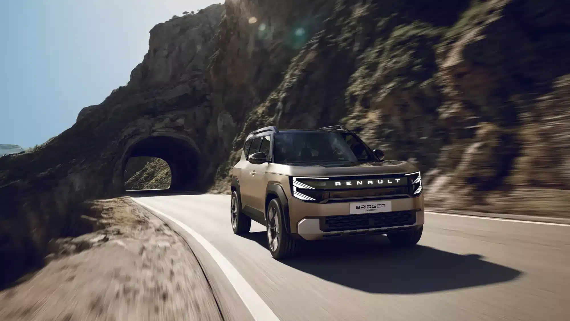Renault Bridger Concept SUV fährt dynamisch vor felsiger Kulisse auf einer Straße mit Tunnel.