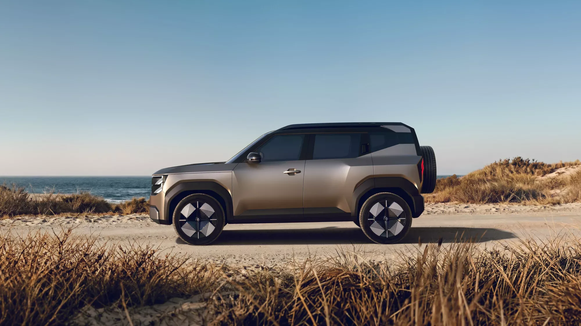 Seitenansicht des Renault Bridger Concept SUV auf einer sandigen Küstenstraße vor Meer und Dünen