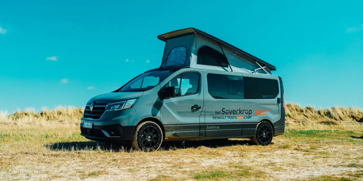 Renault Trafic BS-Camp Campervan mit geöffnetem Aufstelldach steht auf einer Wiese unter blauem Himmel